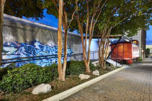 Photo of Kinetic's exterior featuring graffiti art on the boxcar, bushes, trees, and the caboose.